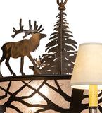 A rustic metal deer and tree silhouette light fixture casting warm light onto a textured beige shade, shown next to a matching lamp on a white background.